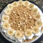 Fresh banana cream pie with graham cracker crust, topped with sliced bananas, chopped nuts, and crushed cookies for a delicious dessert. Perfect for family gatherings and celebrations.