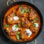 Savory chicken curry with a vibrant, spiced tomato-based sauce, garnished with fresh cilantro and dollops of yogurt, served in a cast iron skillet. Perfect for hearty, flavorful meals.