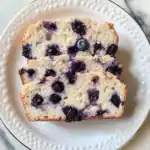 Fresh blueberry bread with ripe blueberries and a soft, moist crumb on a decorative white plate. Perfect for breakfast, brunch, or snack, this homemade blueberry bread recipe promises a deliciously fruity flavor.